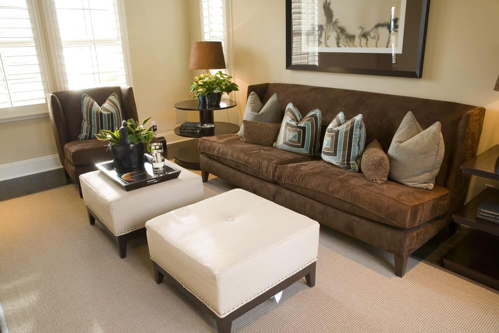 紧凑的客厅，深色摩卡椅和无扶手沙发，与白色单扣簇绒双脚垫形成对比。