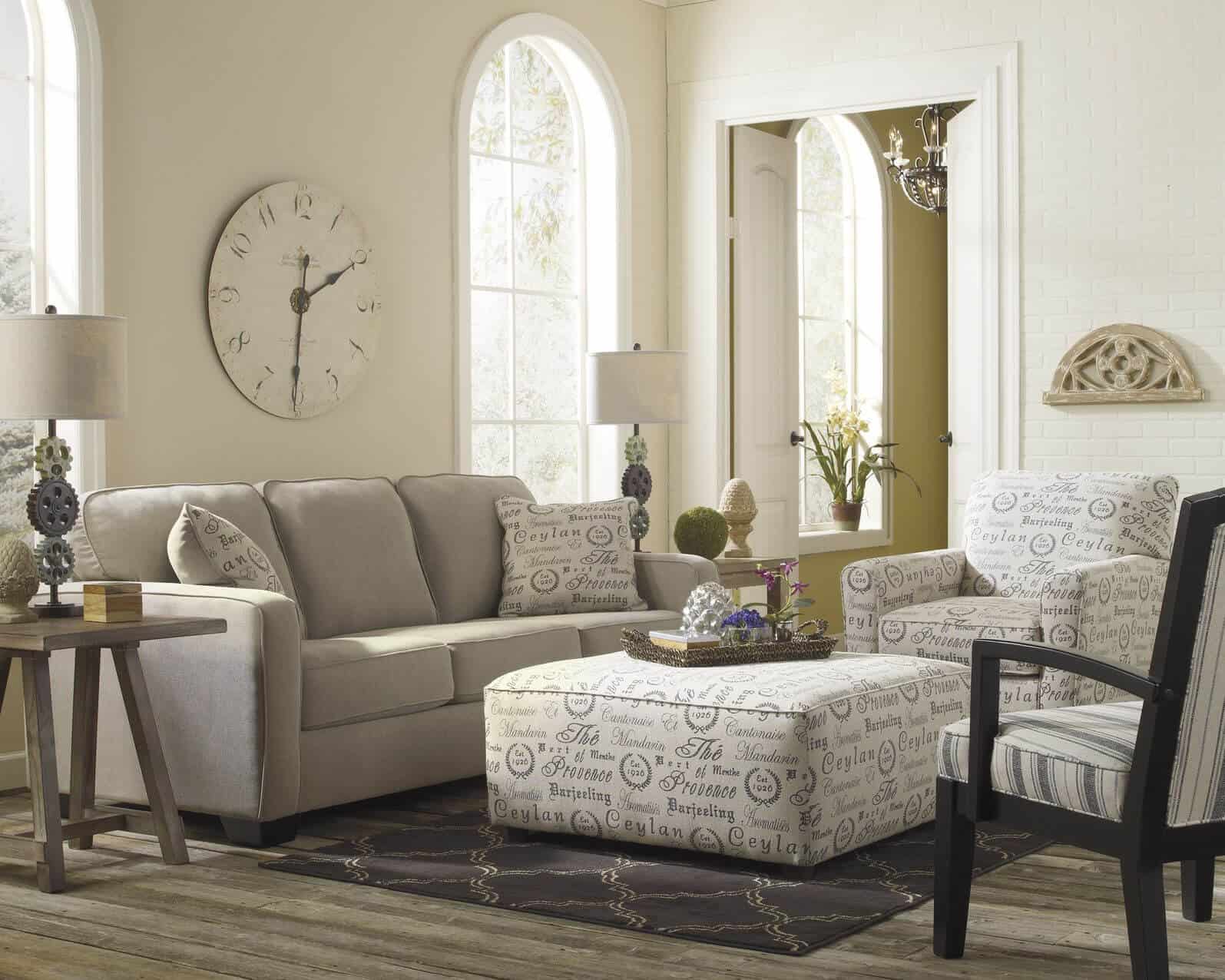 浅色调的客厅位于灰色硬木地板之上，中性灰色沙发旁边是文本图案的白色扶手椅和匹配的方形靠垫。