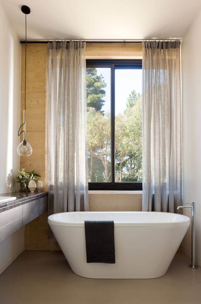 浴室的特色是靠近窗户的白色底座浴缸，左边的柜台上是厨房瓷砖的延续。