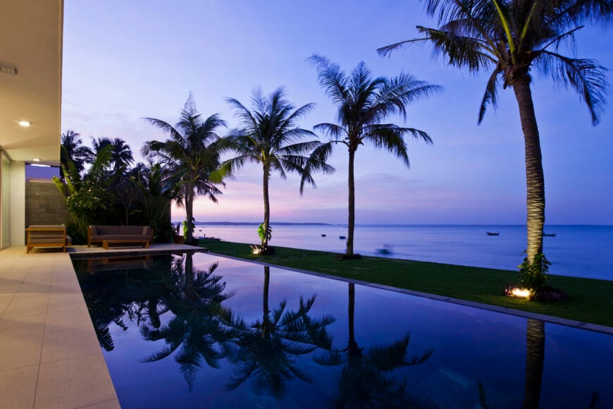 从一个无边泳池的角度看，展示了海洋和棕榈树的平静倒影。