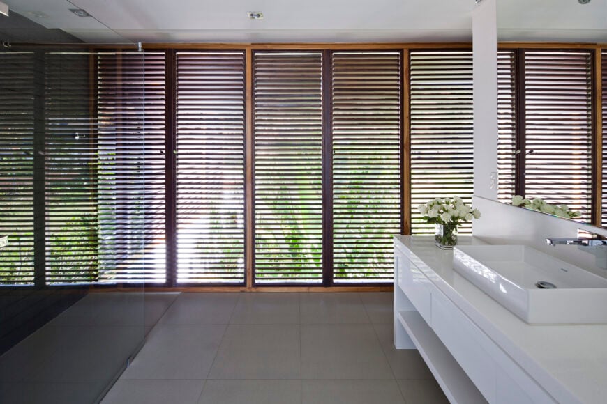 百叶窗提供的隐私和自然光的结合使上层浴室成为重要的组成部分，以光滑的白色橱柜和容器水槽为特色。