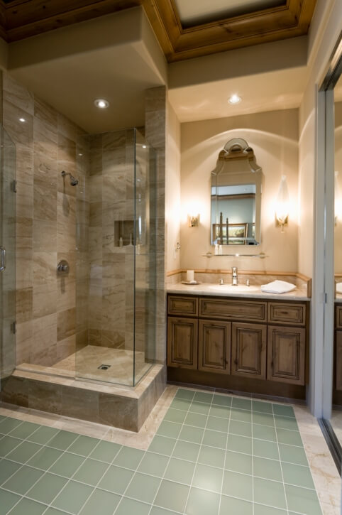 在这间舒适的浴室里，蓝绿色地砖与米黄色大理石和深色色调的木质梳妆台形成对比，设有大型玻璃门淋浴间和木质天花板装饰。