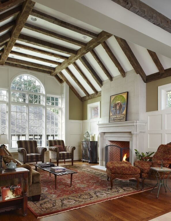 传统华丽的客厅，包括木框架的椅子和沙发，硬木地板上的图案区域地毯，以及白色的石头壁炉，在白色的天花板下，有天然木材裸露的横梁。