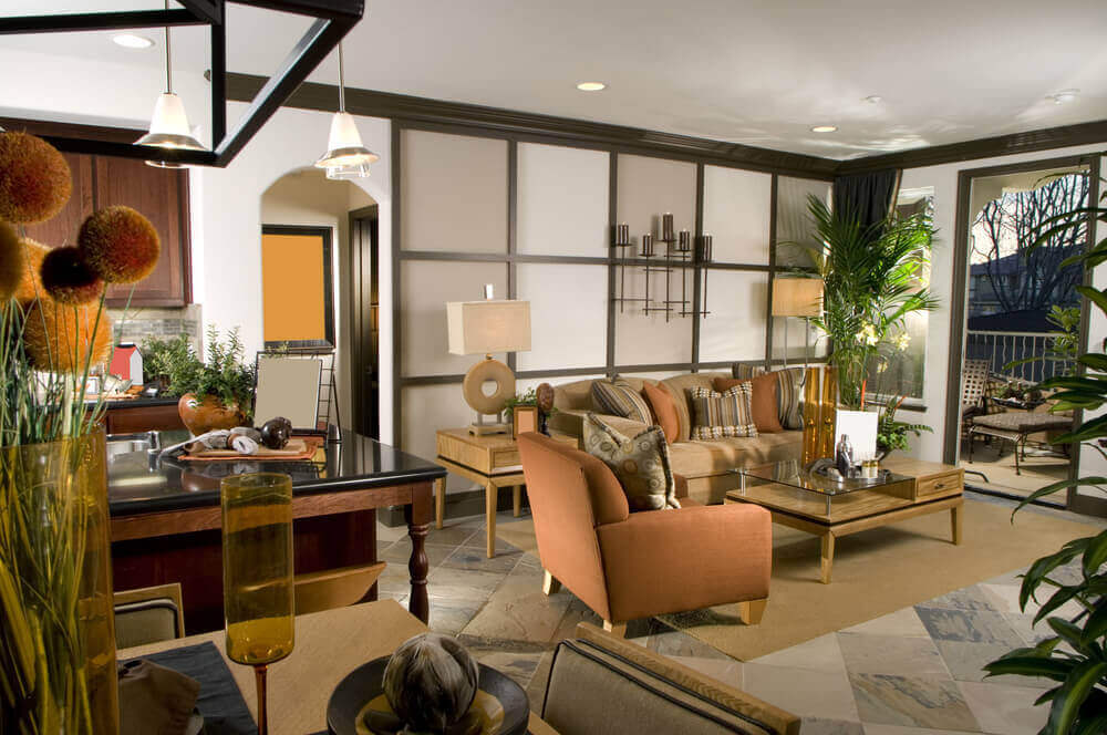 舒适的客厅具有当代风格，双水平玻璃和天然木材咖啡桌在中心，米色和橙色的座位在轻木瓷砖墙前。石材地板支撑着天然材料，左侧是餐厅和厨房空间。