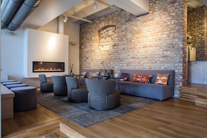 深色天然硬木地板搭配砖墙和白色壁炉环绕在这个工业风格的客厅里。深灰色的沙发和圆形椅子站在中间匹配的图案地毯上。