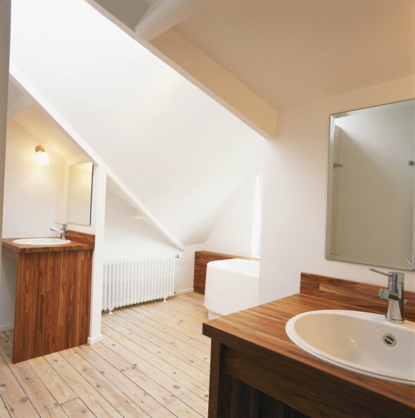 这间浴室设有一对带有白色水槽的天然木质梳妆台，侧面是一个独立的浴室空间，在倾斜的天花板下，浅色硬木地板上有天窗。