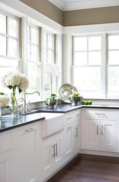 白色木橱柜和黑色台面定义了厨房，无处不在的窗户环绕着厨房，提供充足的阳光和视野。