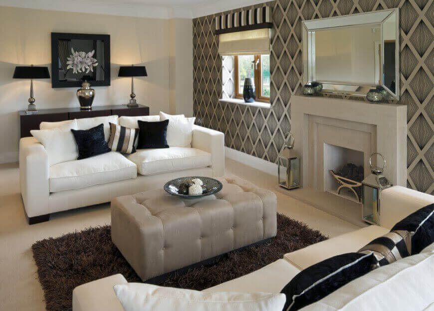 现代风格的客厅设有白色沙发和深色装饰枕头，面向矩形灰色软凳。大理石壁炉周围环绕着详细的墙壁图案。