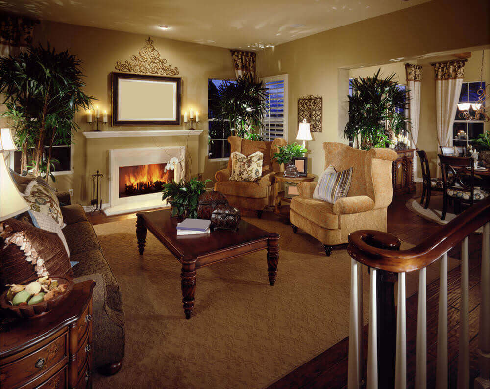 这间客厅设有一对金色的卷臂椅，面对着棕色的碎花沙发，上方是郁郁葱葱的深色木咖啡桌。