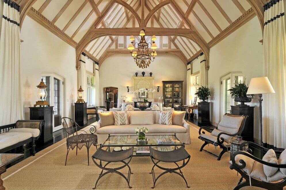 精致平衡的客厅摆放着浅色和深色的家具，在深色木地板上伸展的米色区域地毯上，在拱形白色天花板下，有天然木材裸露的横梁。