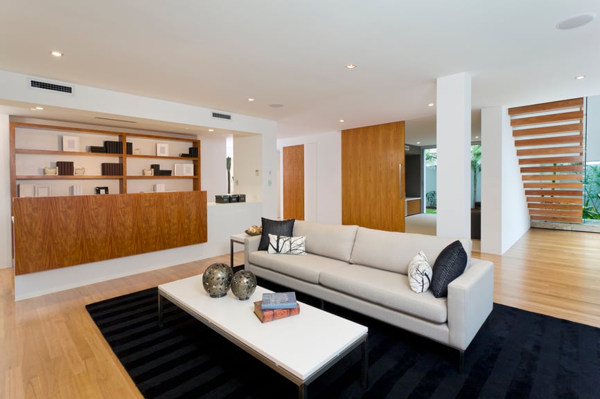 高对比度的客厅将黑色地毯和米色当代皮革沙发与浅色天然木地板、书架、门和楼梯安装在纯白色的墙壁和天花板上。