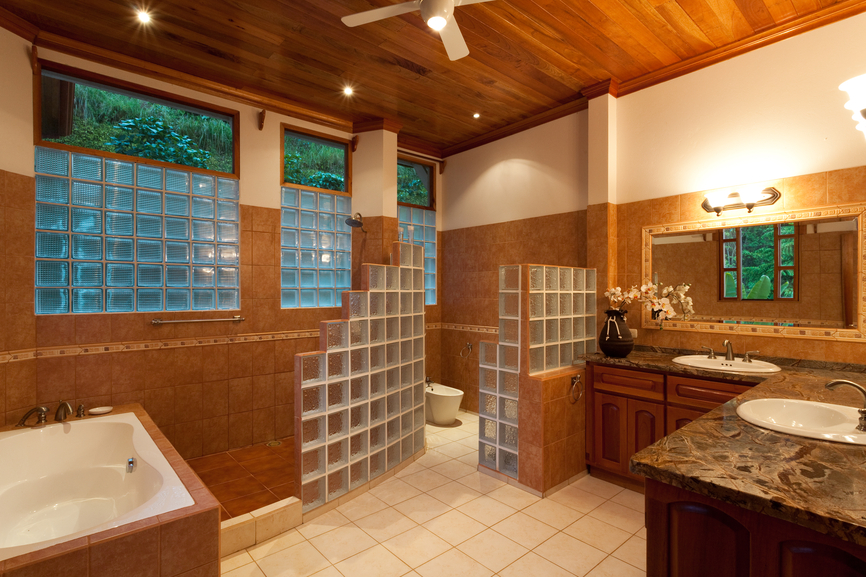 复杂，郁郁葱葱的浴室站在巧妙的砖立方体墙之间的淋浴，厕所，和梳妆台空间。在硬木天花板下，深色大理石台面下的深色木质橱柜，浅棕色瓷砖和白色地板增添了各种质感。