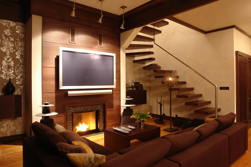 现代风格的客厅设置深棕色的组合家具和木制咖啡桌，壁炉前有光滑的天然木镶板环绕。右边的黑色“浮动”楼梯与整个装饰风格相匹配，包括造型和门框。