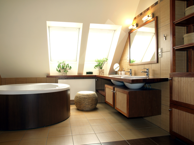 禅宗风格的极简主义浴室以深色木材包裹的独立式浴缸为特色，浮动的台面和匹配的木质较低的橱柜，周围都是米色和棕色的瓷砖。