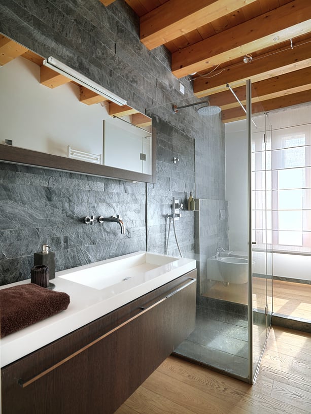 独特的黑色石墙支撑着漂浮的深色木梳妆台和白色台面，浴室里的玻璃淋浴间配有天然硬木地板和裸露的横梁。