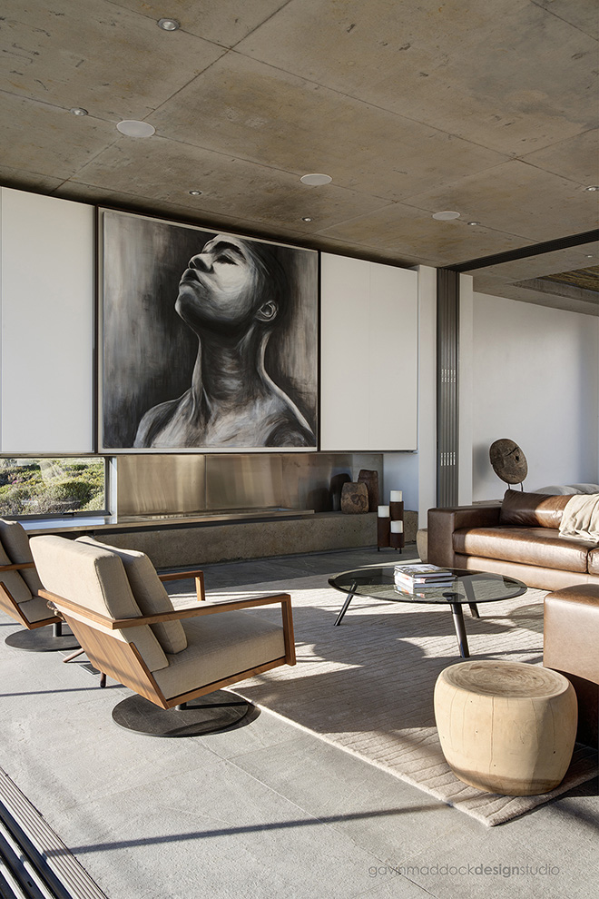 大型艺术品耸立在客厅上方，沙土色调的区域地毯定义了空间。当代棕色皮革组合家具加入一对现代木材和织物转椅围绕现代玻璃咖啡桌。