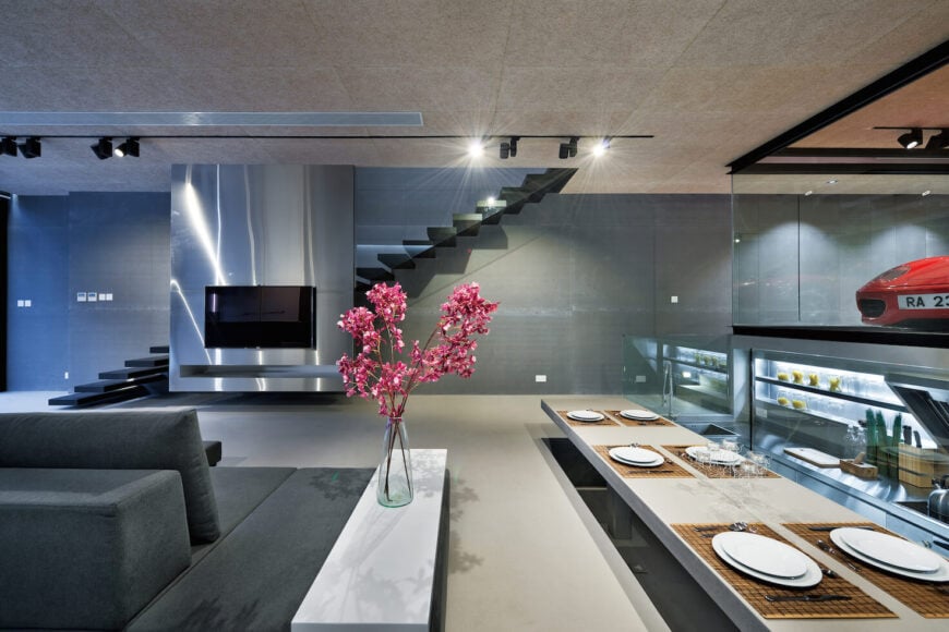 垂直的视角显示了降低的厨房区域和餐桌设置在一层，而玻璃笼罩的楼梯漂浮在对面的墙壁上，后面是金属介质板。