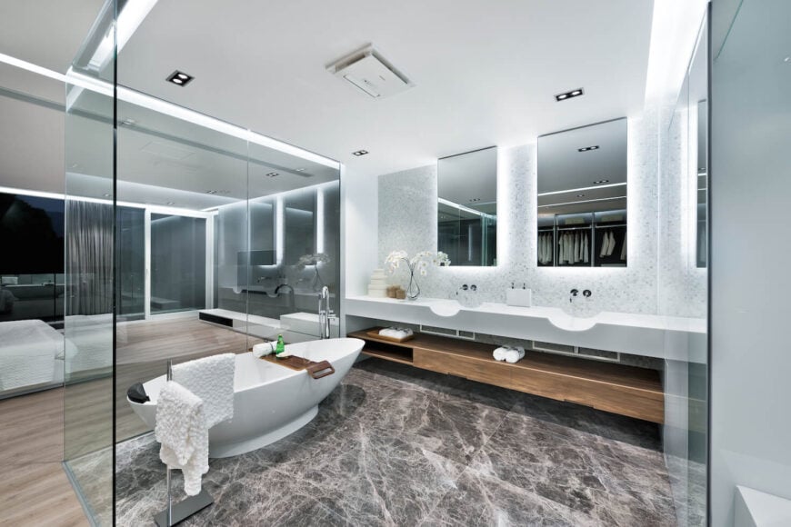 深色大理石地板浴室包含白色底座浴缸和白色双梳妆台下面的天然木材储藏室。