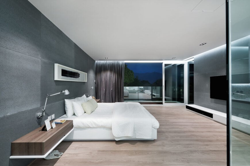 主卧室设有玻璃幕墙阳台的广阔视野，以及白色床两侧的壁挂式木架子。