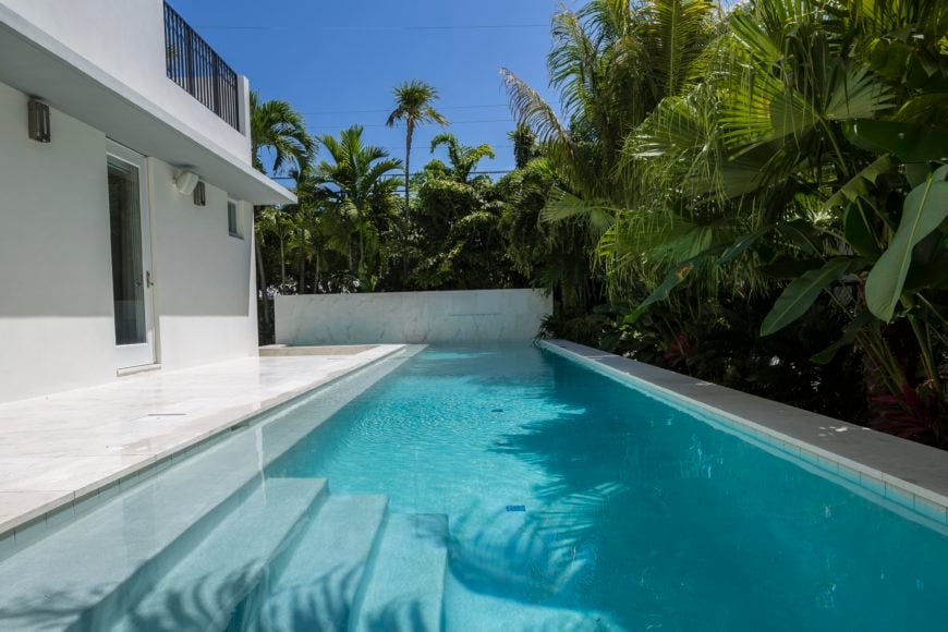 泳池的长度突出了原始大理石和白色房屋与周围茂密的棕榈花园之间的对比。