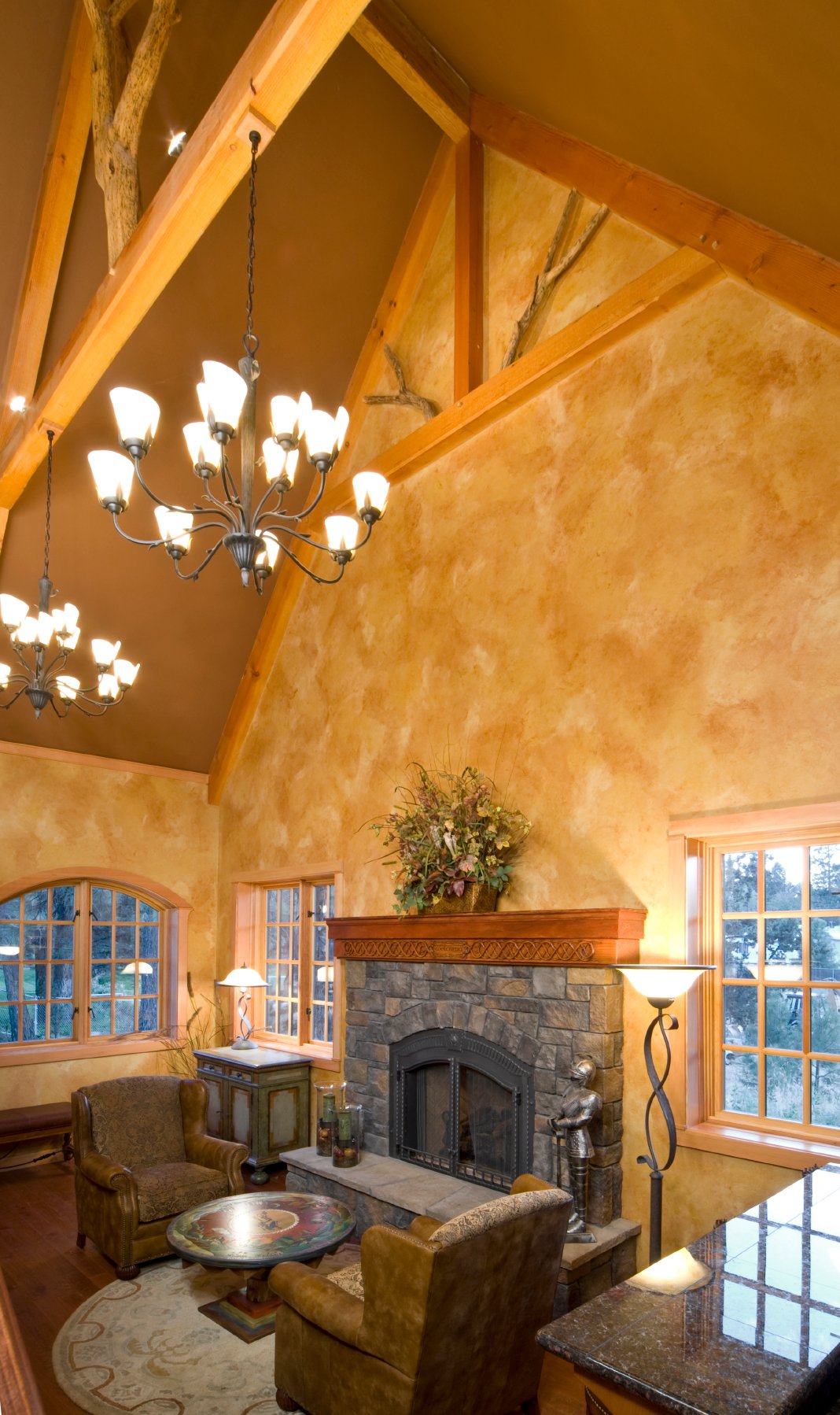 高耸的拱形天花板和裸露的天然木梁在这个舒适的空间上方盘旋，在一对皮革卷臂椅和涂漆的圆形咖啡桌前，有一座巨大的石头壁炉。