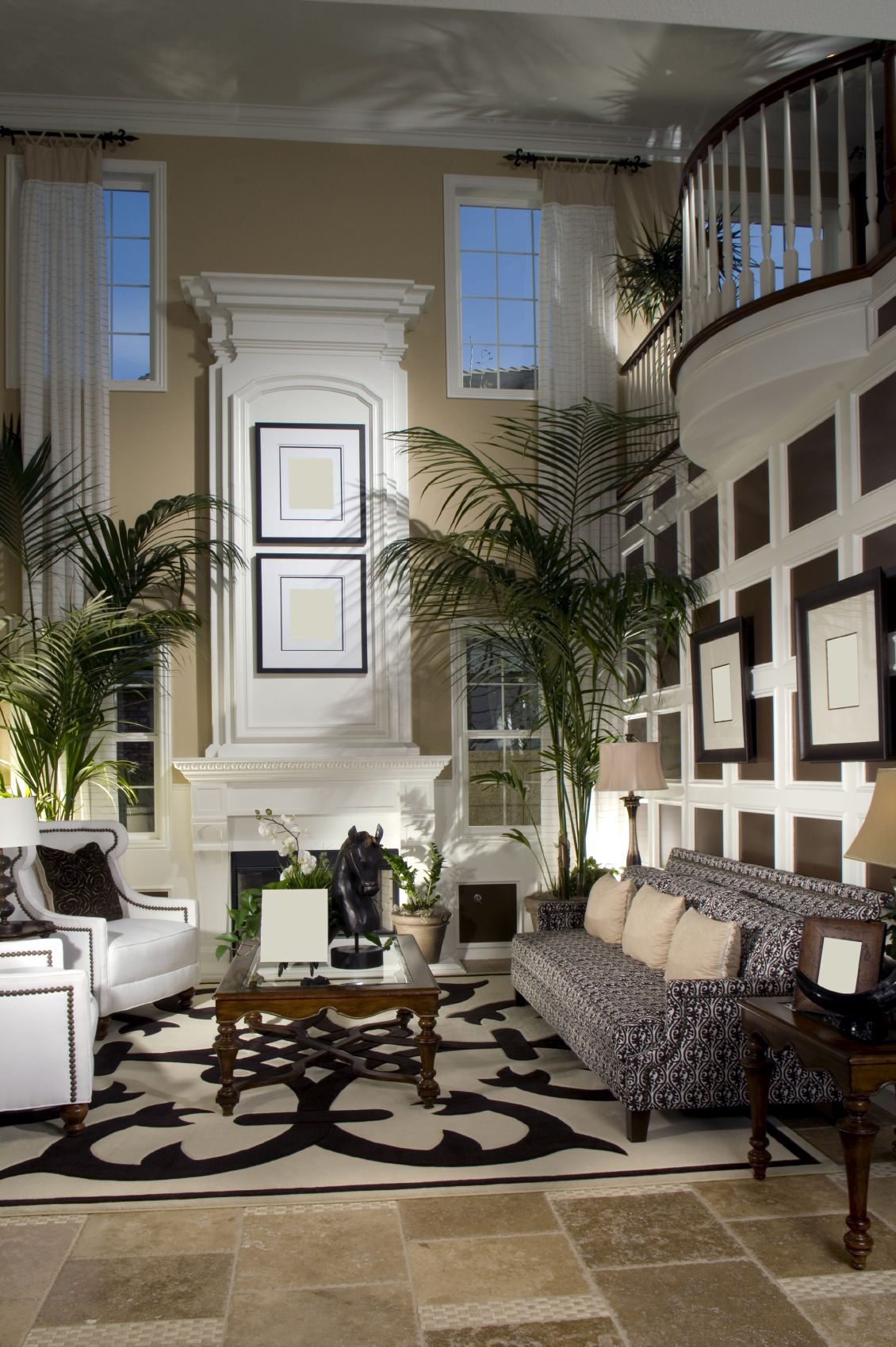 木栏杆的t台俯瞰着这间客厅，有图案的沙发和两把白色椅子正对着玻璃面深色木咖啡桌，米色石材地板上铺着黑白相间的设计区域地毯。