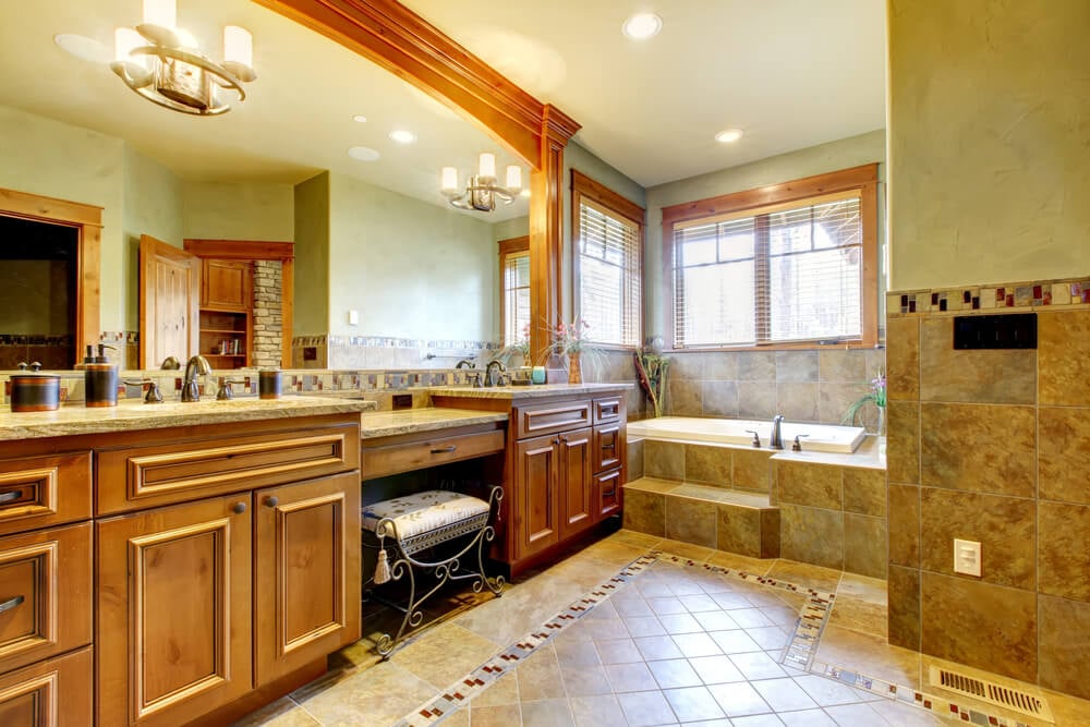 整个浴室的温暖色调包括大地色调瓷砖地板和浴缸环绕，天然木质梳妆台柜和镜子环绕，以及灰色大理石台面。
