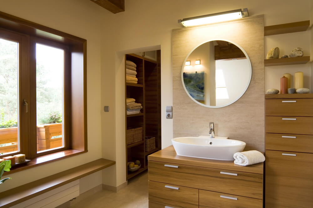 复杂的主浴室以郁郁葱葱的天然木质梳妆台为特色，整个浴室都配有配套的木质搁架。白色容器水槽位于圆形镜子下方，后面的单独区域设有存储空间。