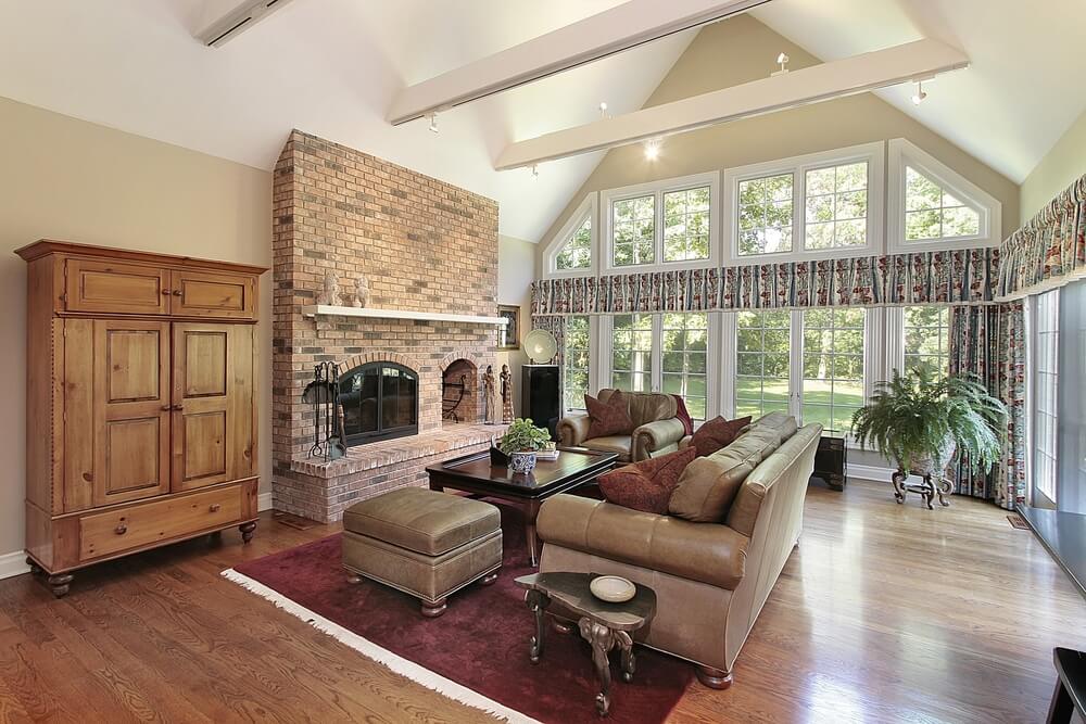 这间客厅的传统风格包括内置木储物柜的红砖壁炉，硬木地板上的天然木柜，以及围绕深色木桌的棕色皮革沙发。全高的窗户覆盖着后面的拱形墙。