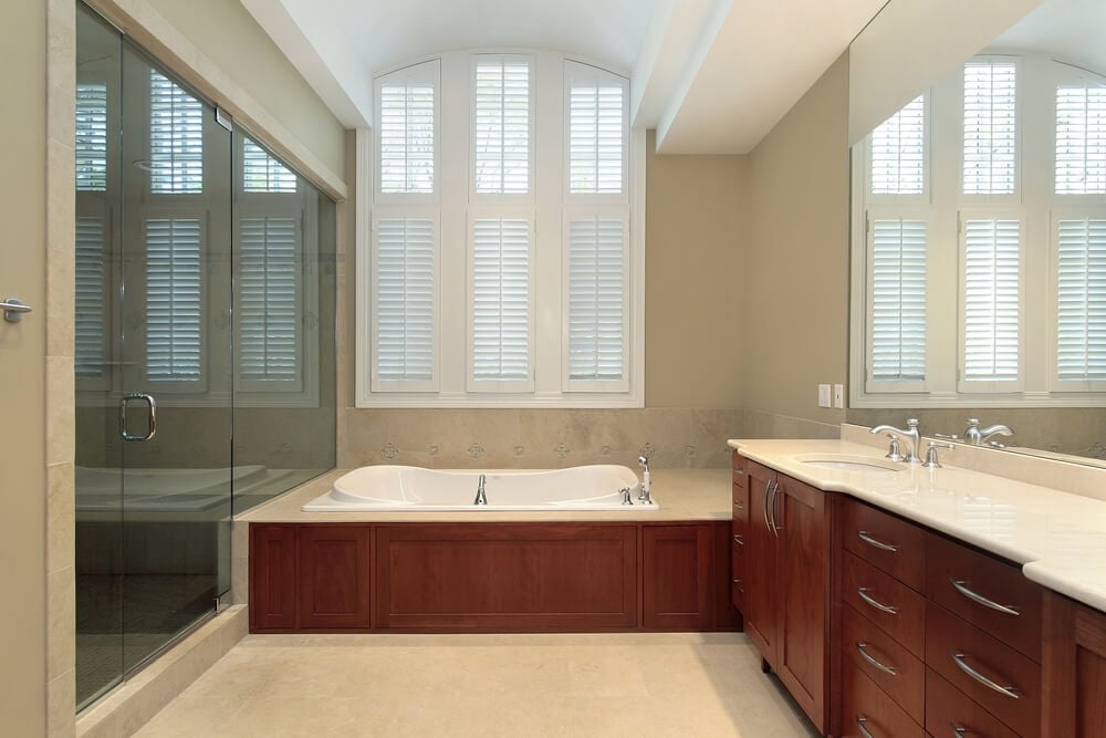 亲密的米黄色色调的浴室，设有光滑的暖木橱柜和浴室环绕，轻质大理石台面，瓷砖地板，玻璃入口淋浴在左侧。