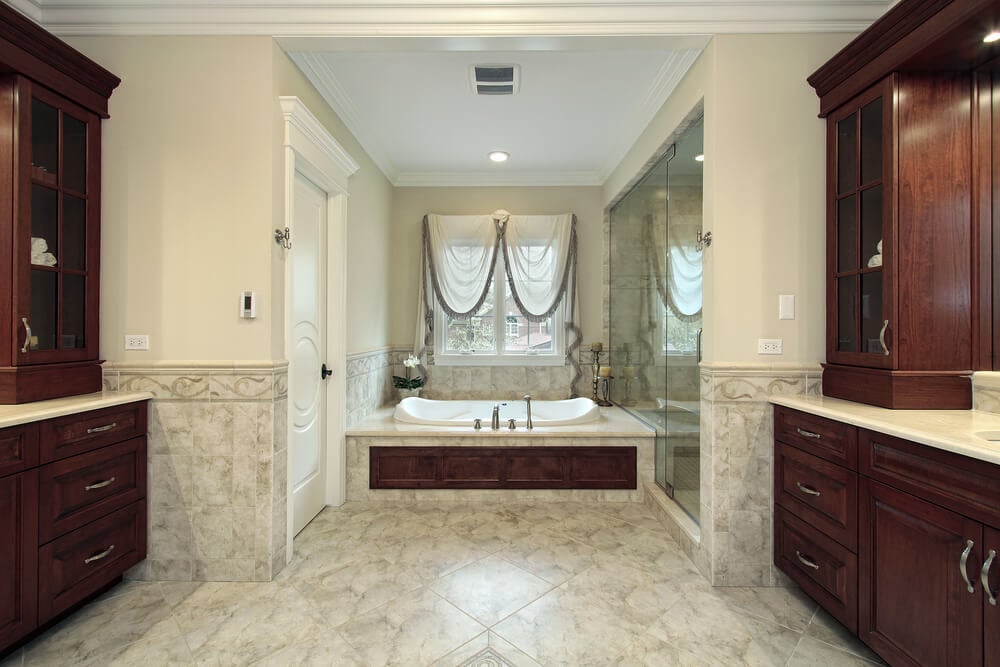 豪华的主浴室沐浴在有图案的大理石上，有两个黑色木材色调的大梳妆台和白色大理石台面，加上大型全玻璃浴室和浴缸，周围环绕着配套的木板。