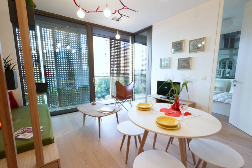 开放的起居空间中央摆放着餐桌和配套的圆形椅子，自然光线透过滑动玻璃后的阳台。