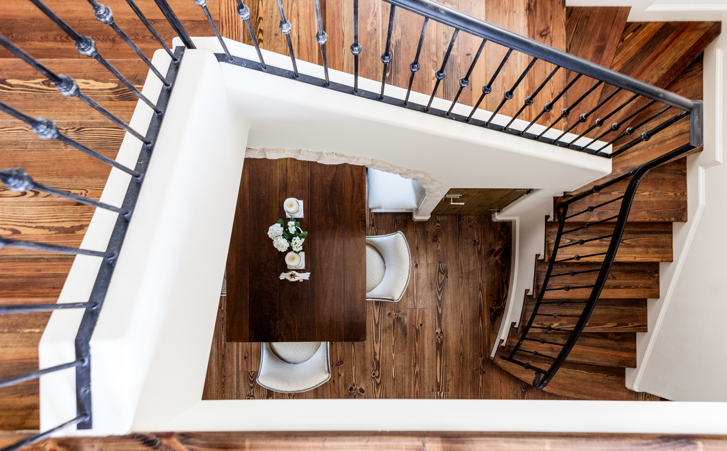 垂直向下看一楼，楼梯上有大片丰富的天然木材色调，与白色墙壁和锻铁栏杆形成鲜明对比。