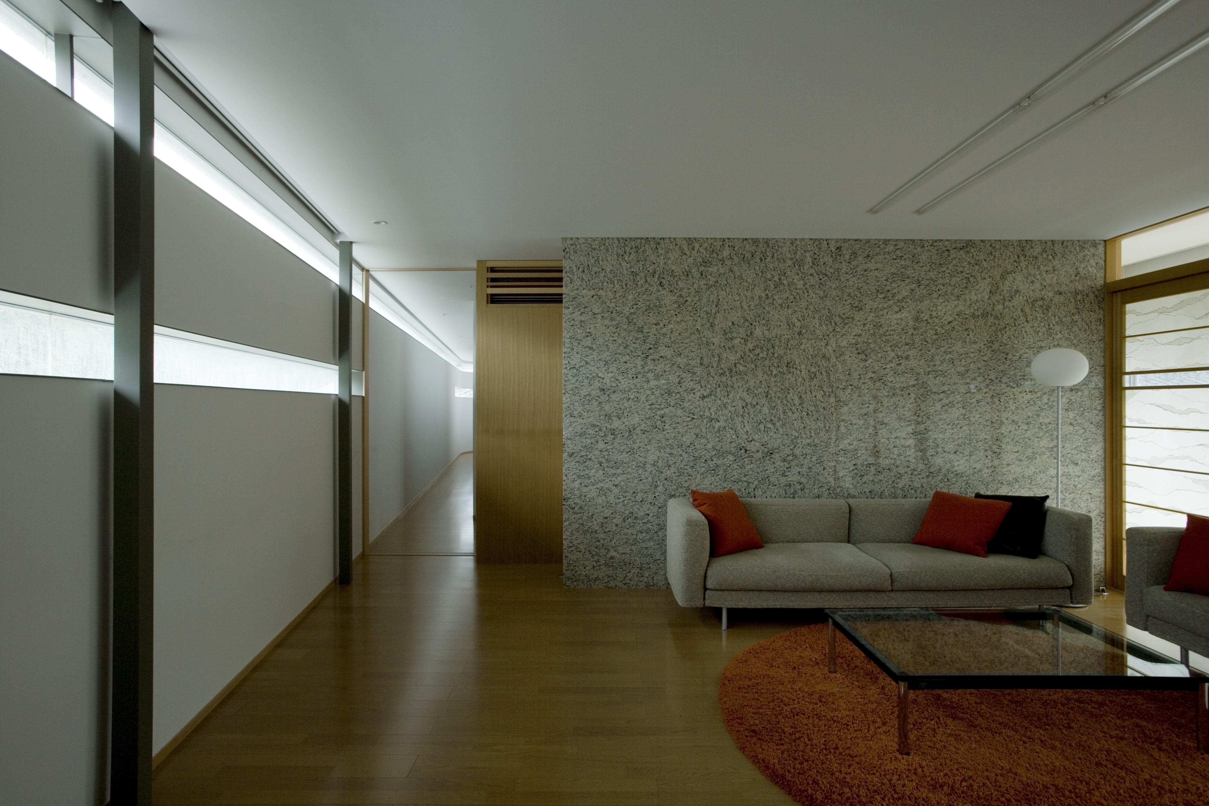 客厅的特色是现代灰色沙发环绕着一个大玻璃咖啡桌，上面是圆形橙色地毯。硬木地板贯穿整个住宅，左侧外墙上的开缝窗贯穿整个住宅。