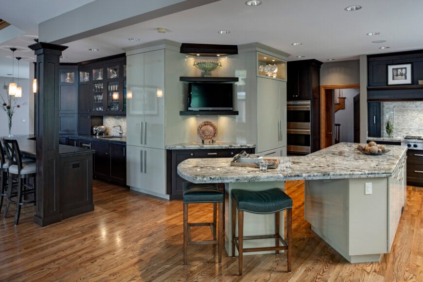 宽敞的过渡厨房以右侧的l形岛形为特色，设有完整的环绕式用餐空间，深色木材和浅灰色的高对比度橱柜，覆盖天然硬木地板。