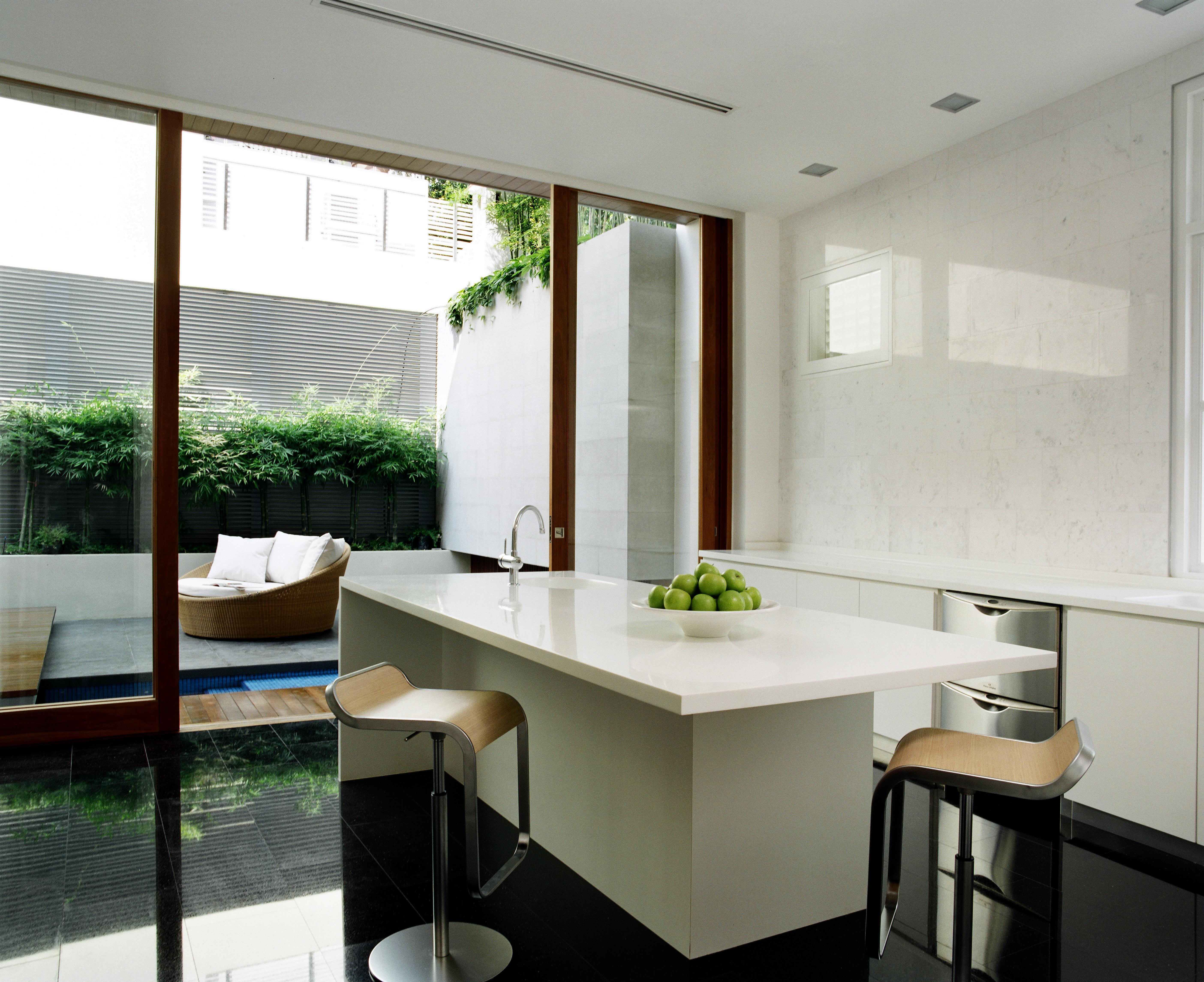 黑色瓷砖地板和白色台面的对比定义了舒适、简约的厨房空间。岛上的特色用餐空间在一对金属和良好的凳子上，而露台上的圆形柳条座椅可以通过滑动玻璃板看到。