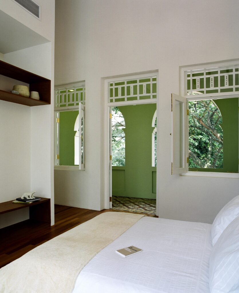 卧室全白色，深色硬木地板，墙上有一对天然木架子，窗户通往绿色的有盖露台大厅。