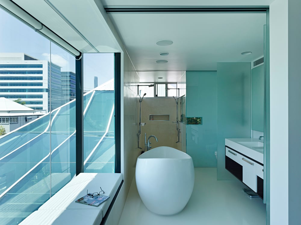浴室以独特的蛋形基座浴缸为特色，周围是多层烟熏玻璃。左侧靠窗的座位位于白色靠垫上，背景是步入式淋浴。