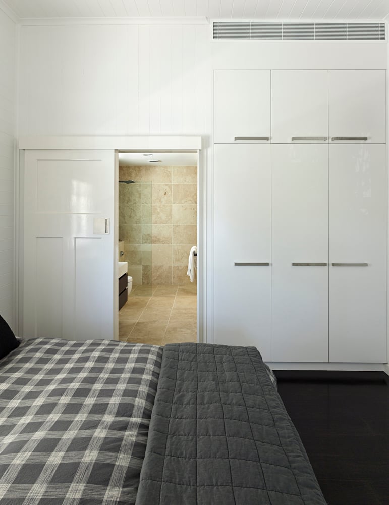 卧室的特点是一系列极简主义的白色橱柜融入墙壁，黑色地板上，滑动木门通往浴室。