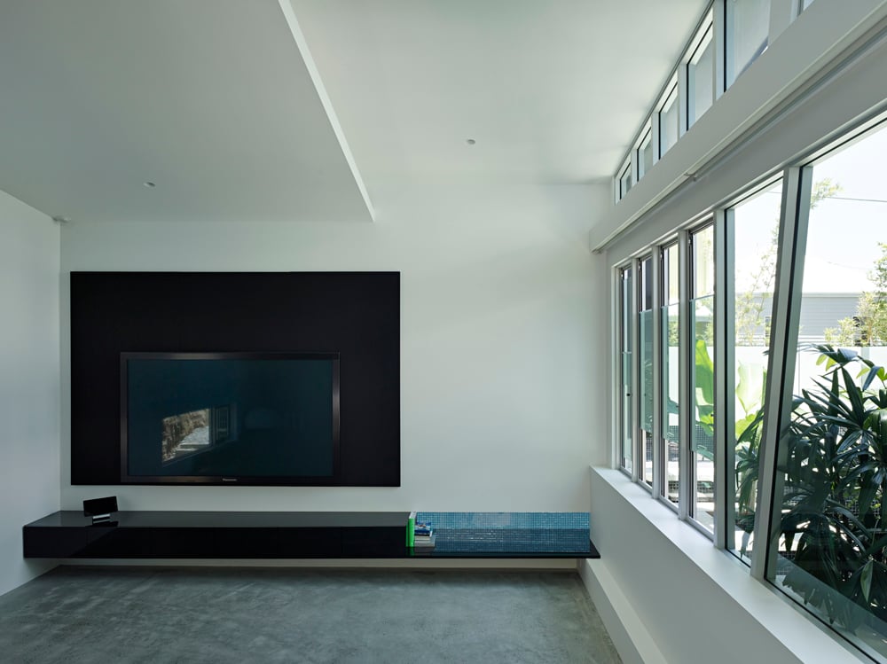 极简设计的客厅以电视的黑色媒体环绕为特色，独特的黑色架子内置于墙壁中。棱角分明的窗框点缀着右侧的玻璃墙，可以看到屋顶花园的景色。