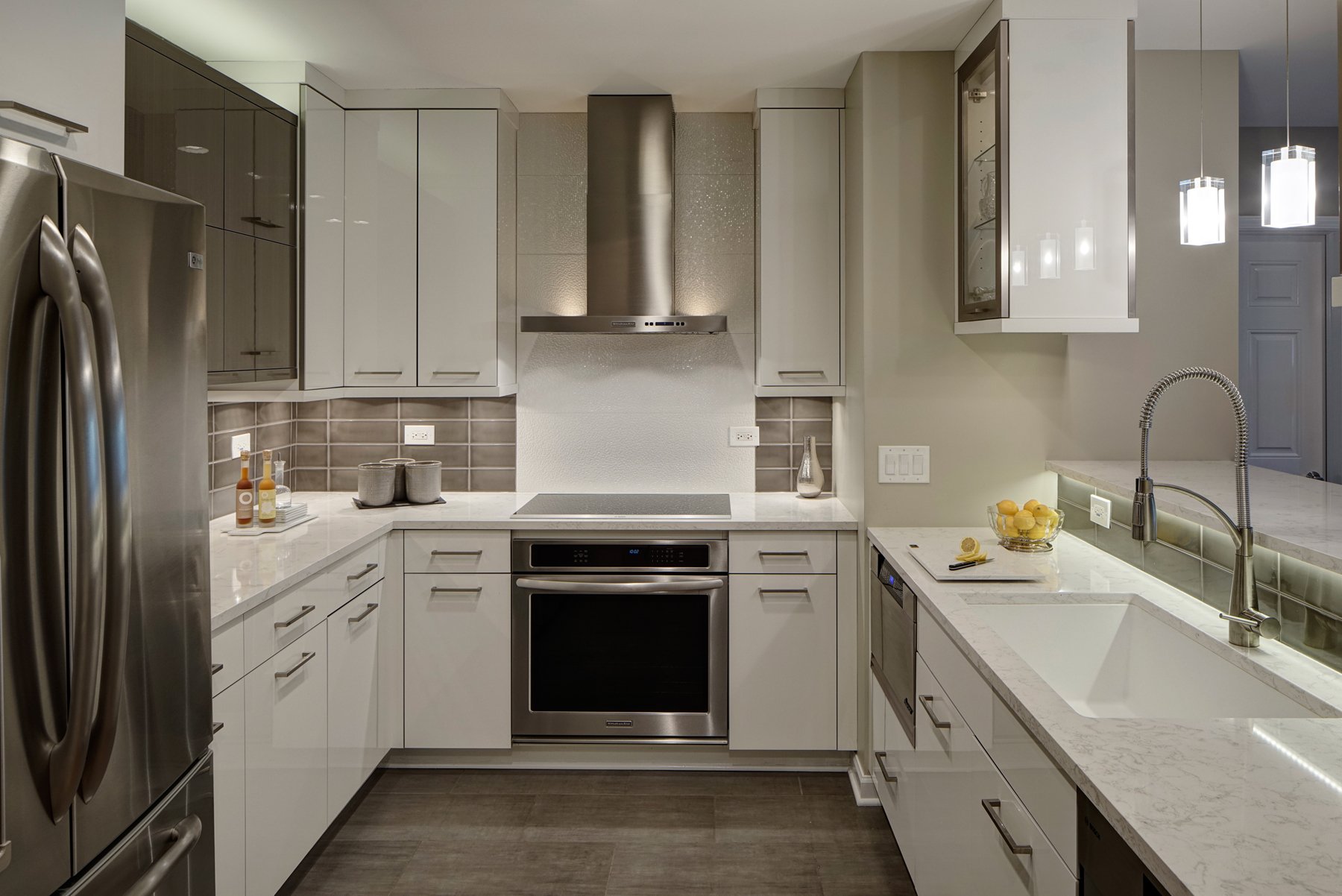另一个现代设计，这个厨房有光泽的白色橱柜，轻大理石台面，拉丝钢电器，以及不亮的瓷砖后挡板。