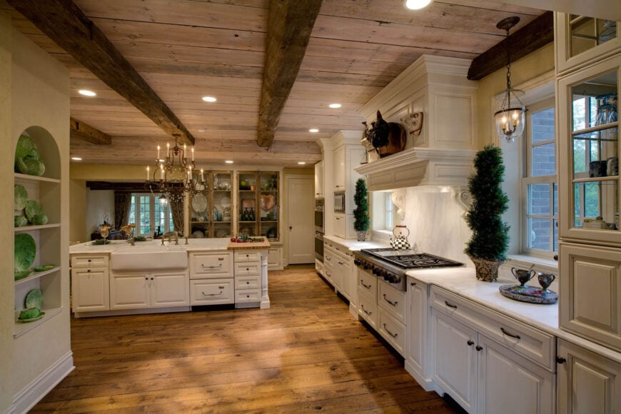 宽敞的乡村风格厨房，白色橱柜和现代电器位于天然木天花板下，横梁外露。白色岛与大型内置水槽位于中心，与砧板表面的一端。