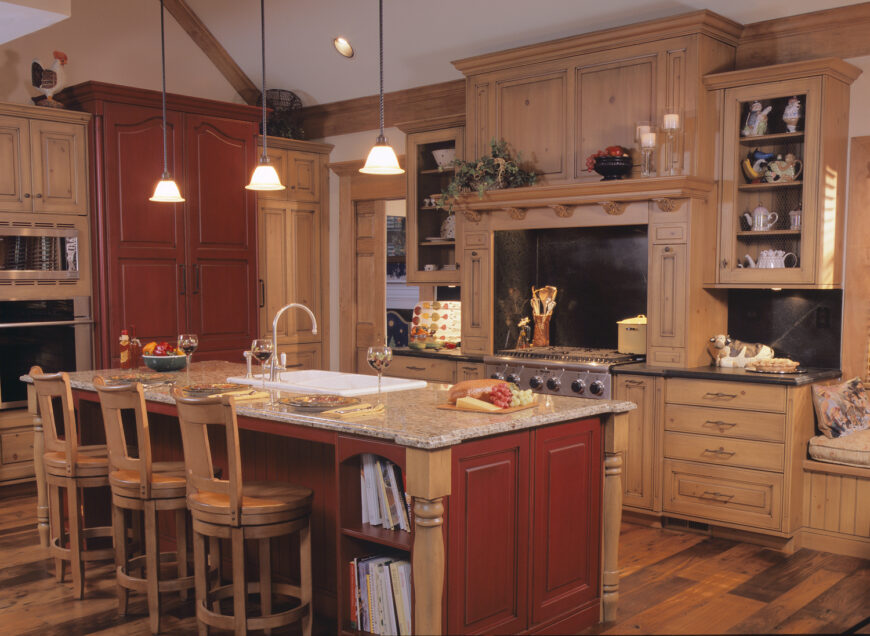 这是另一个传统风格的天然材料厨房。浅色木橱柜搭配深色台面和配套的后挡板，而红色木岛台和单一的全高橱柜强调了中性色调。