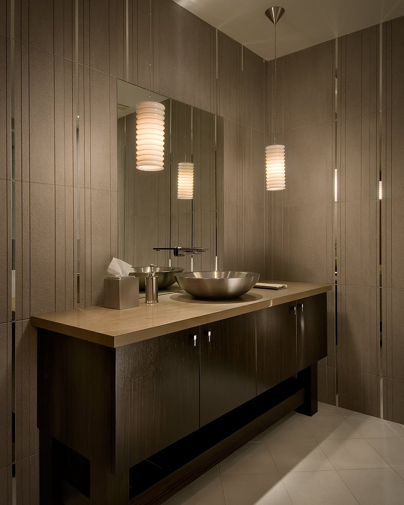 浴室设有一个定制的梳妆台，石英岩板台面上有钢制容器水槽。棕色的瓷砖墙与镜像条交叉切割。