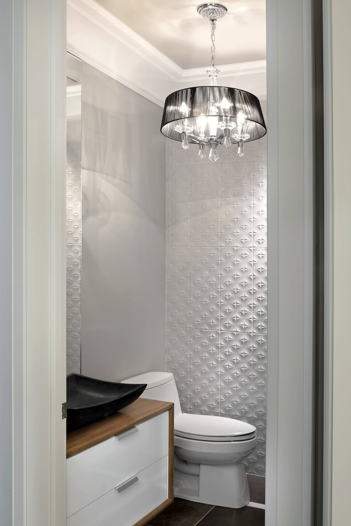 半浴室的特色是这种独特的白色纹理瓷砖墙，以及天然木材包裹的漂浮梳妆台和黑色容器水槽。