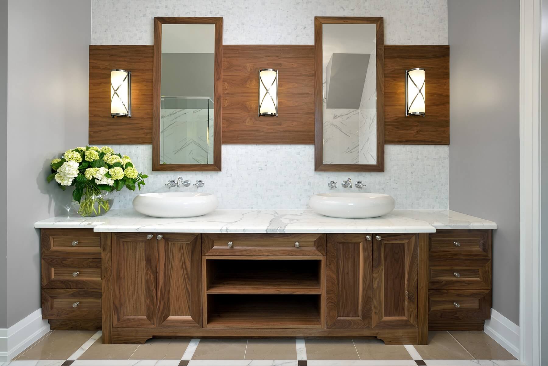 双梳妆台设有大理石台面上的大型白色容器水槽，一对独立的镜子挂在光滑的墙壁上安装的木镶板上。