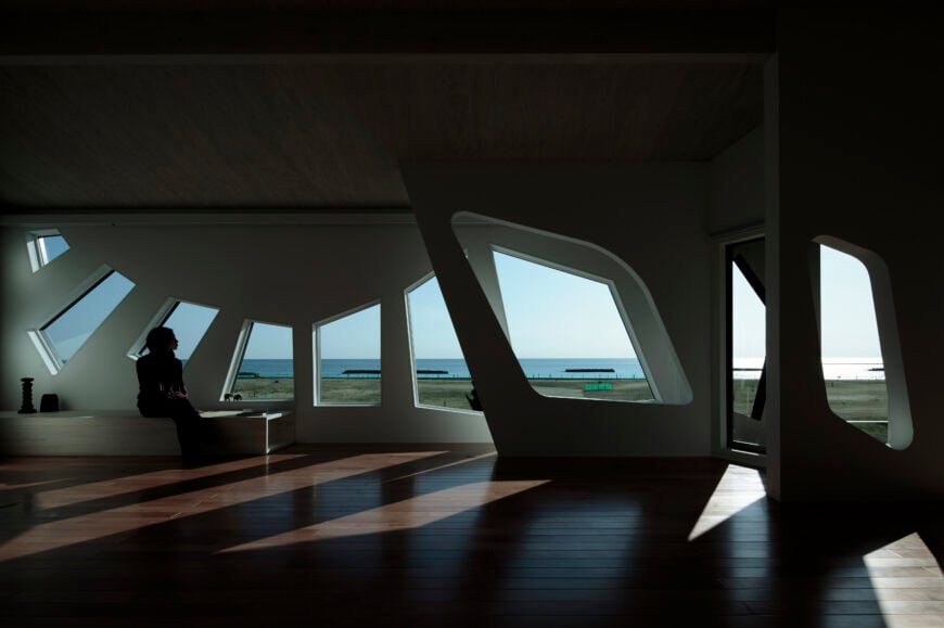 棱角分明的窗户反映在内墙的软边镂空中。左边是一个小的天然木材空间，可以凝视大海。