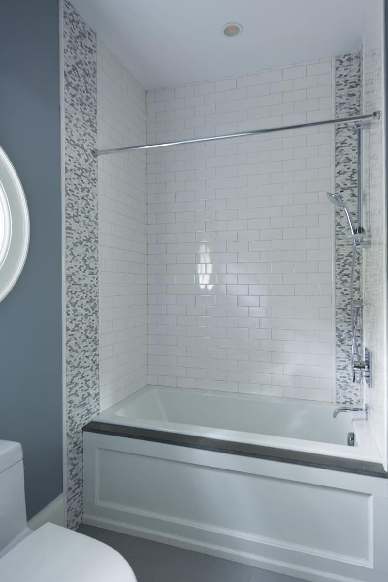 传统的淋浴间和浴室位于白色瓷砖砖空间内，两侧是有图案的微型瓷砖条。