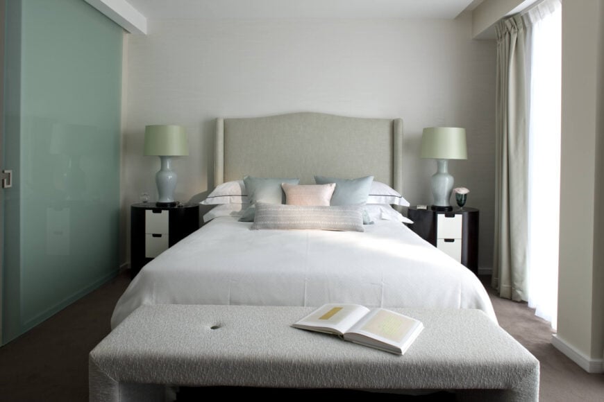 这个次级卧室的特点是混合了家中最柔和的色调，包括白色、天蓝色和浅粉色。床脚有一个大的奥斯曼长凳，而一对现代的深色木材梳妆台和白色抽屉放在床的两侧。