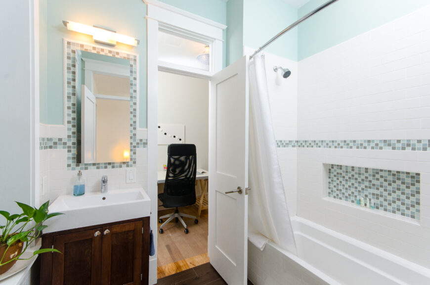 浅色地板通向第二间浴室的深色硬木地板，与深色木质梳妆台相呼应。淋浴和浴缸隔间是白色的地铁瓷砖，吧台和一个小隔间里有少量的蓝色和棕色瓷砖。